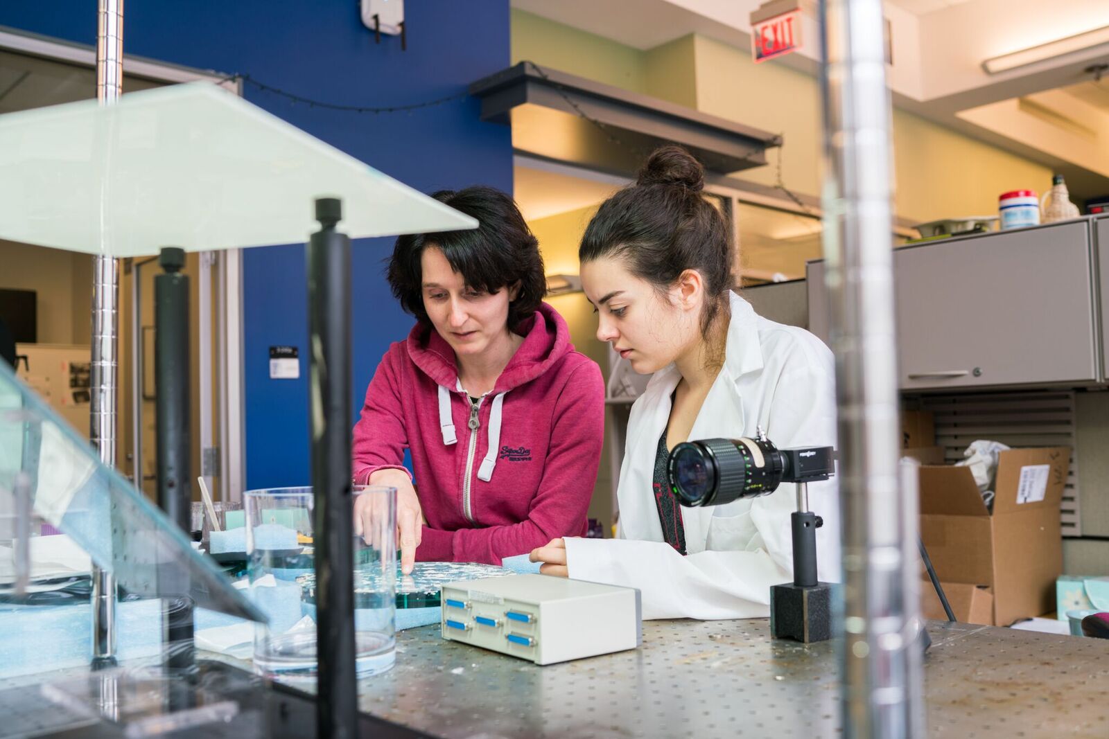 An instructor and a student in a white lab coat look at samples in a lab.