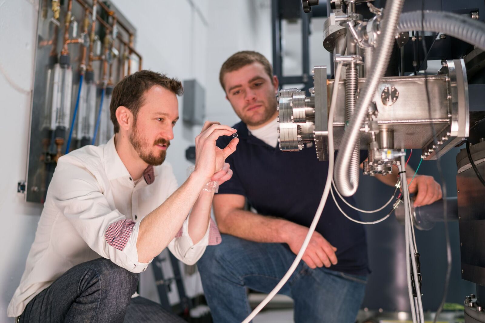 Two people crouch down as they look at a large piece of equipment.