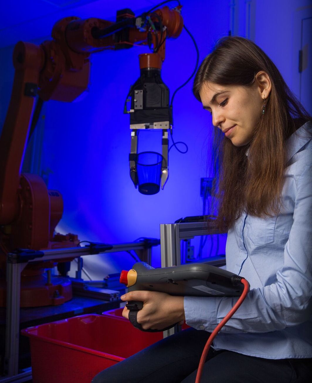 A student looks down at a piece of equipment. In front is a mechanical arm holding a small glass.