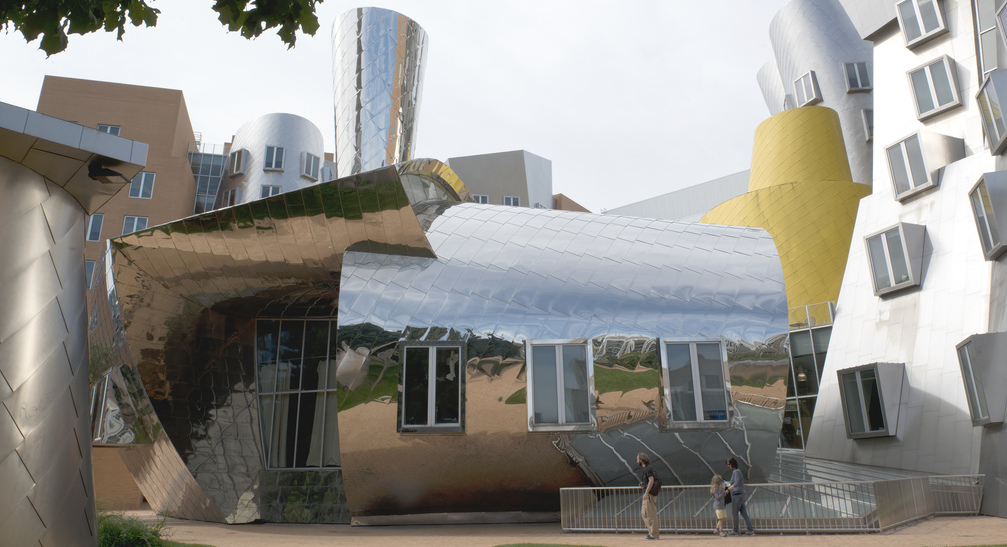 People walk in front of the Stata Center. The middle section is mirrored and has three windows. The off-center architecture of the rest of the building is visible in the background.