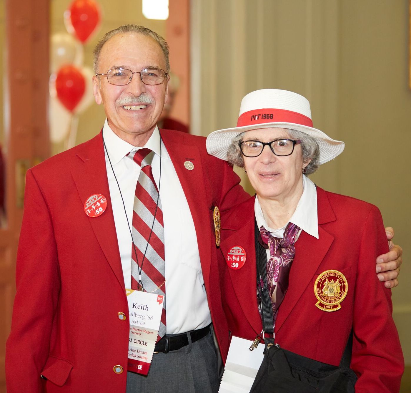 Two alumni wearing red blazers with large pins that say, "MIT 1968."