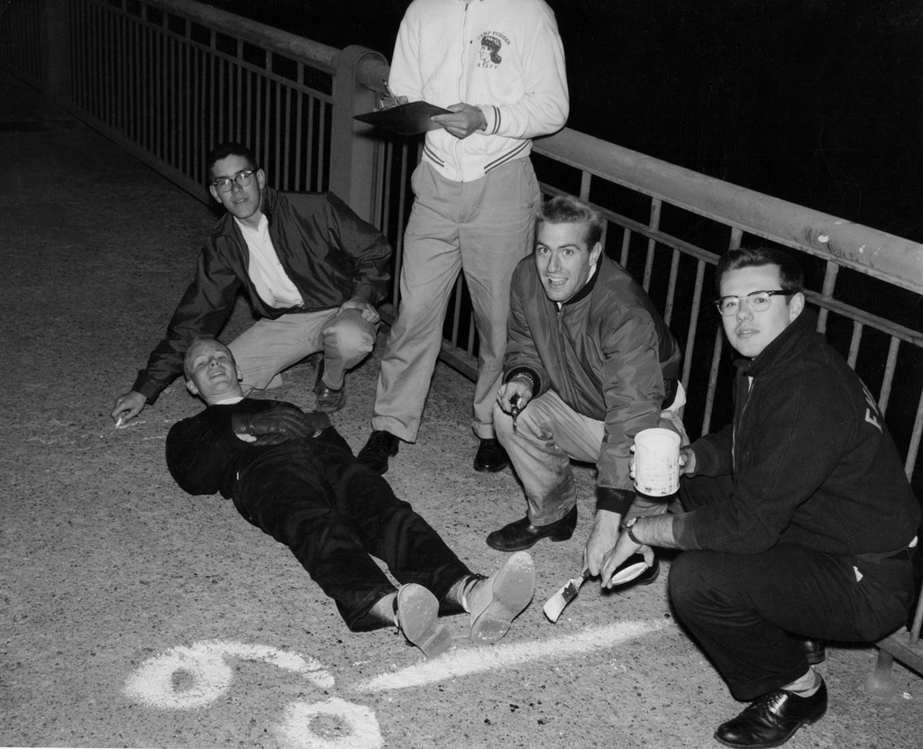 A black and white photo of five students on the Harvard Bridge, with Oliver Smoot lying on the ground.