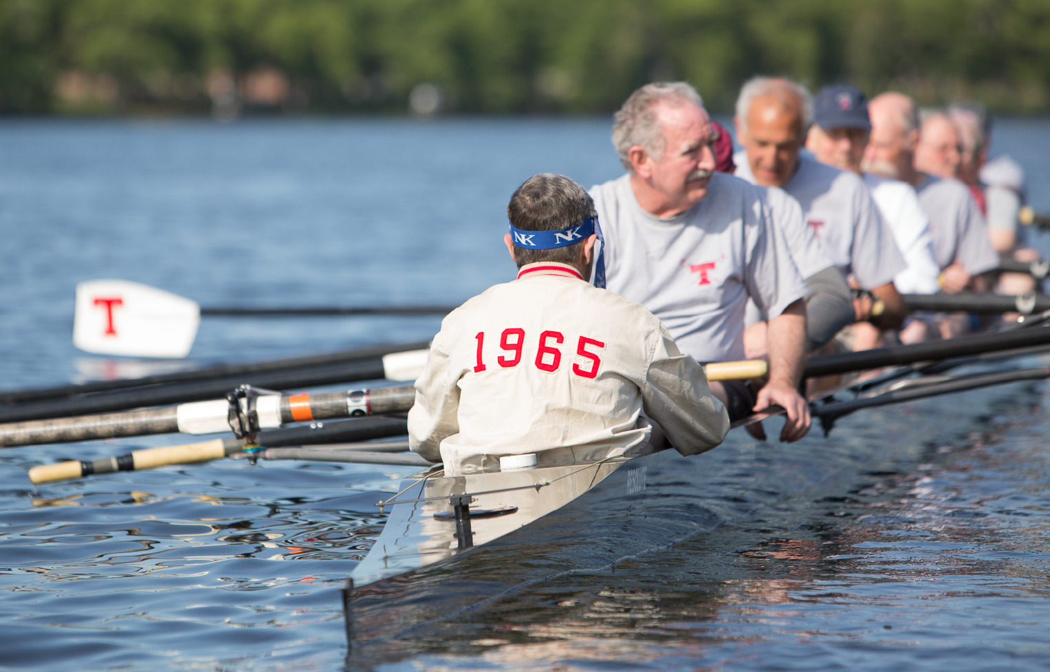 Seven alumni row in a boat. The person in the front of the photo has 1965 on the back of his shirt.