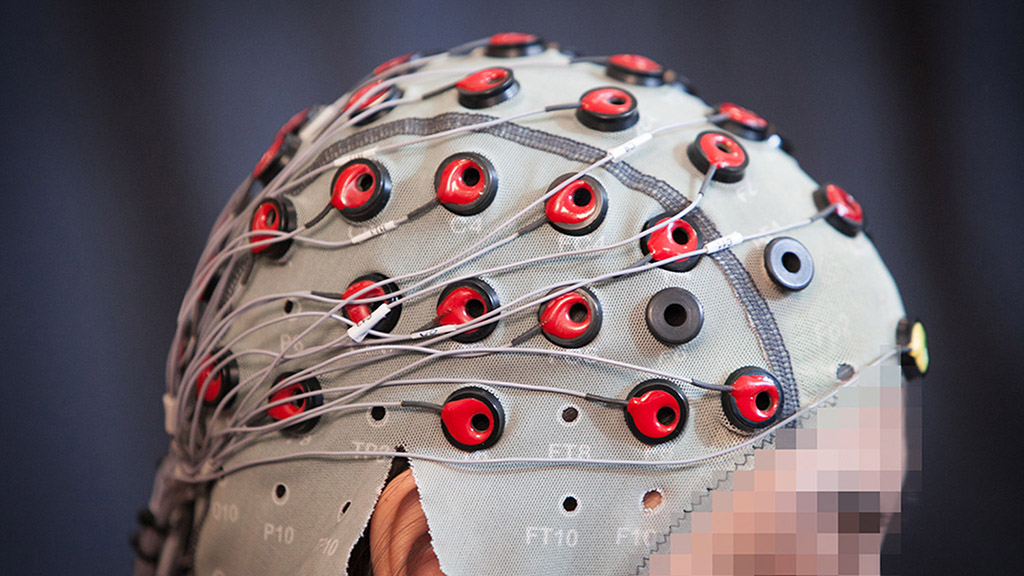 A person wears a head covering with numerous red, round buttons that connect to wires.