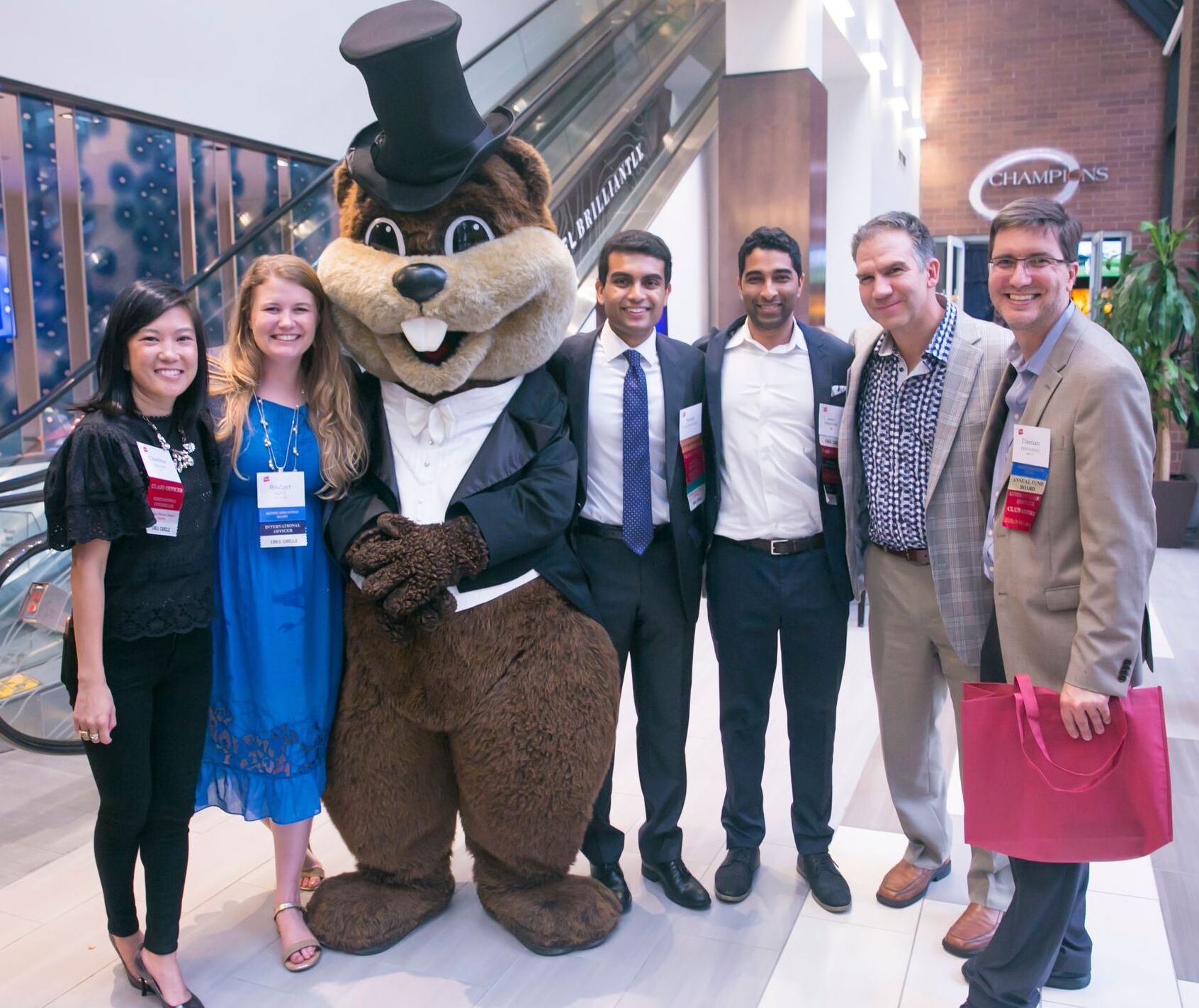 A group of six people pose next to the Tim the Beaver mascot, who is wearing a tuxedo jacket and top hat.