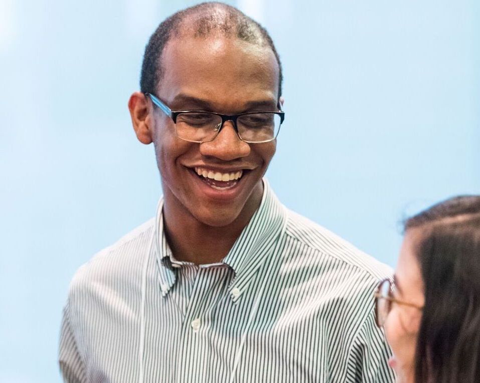 A person wearing glasses smiles at the person he's talking to.