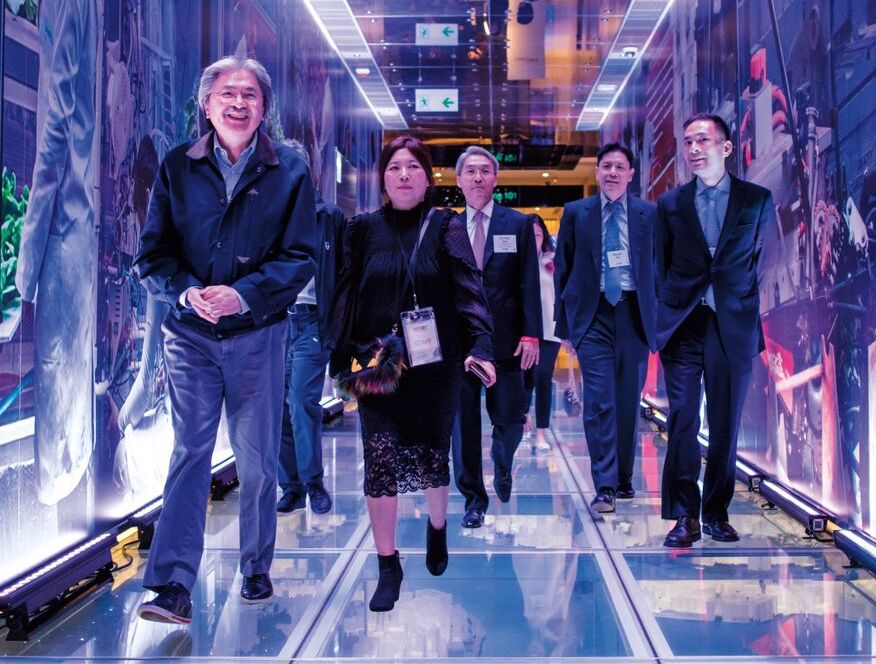 A group of people walking through an illuminated display. There are large images on the walls, and the floor is lit up.